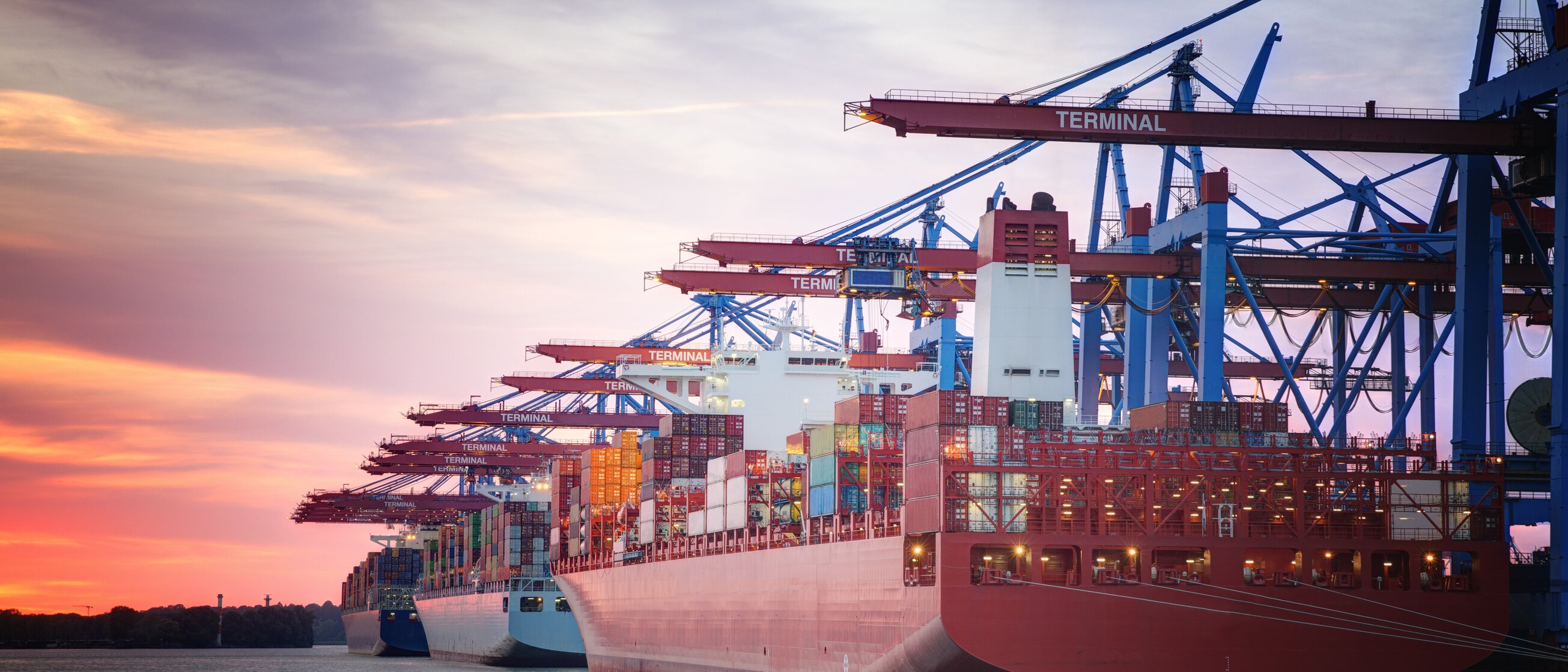 Ein großes Containerschiff wird bei Sonnenuntergang im Hafen von Kränen be- oder entladen.