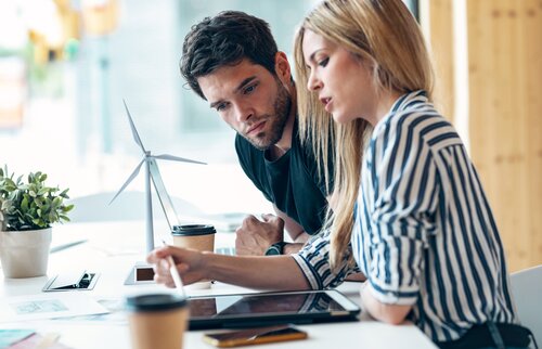 Eine Frau erklärt einem Kollegen etwas auf dem Tablet, während beide über nachhaltige Energiekonzepte arbeiten.