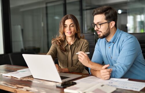 Zwei Personen sitzen gemeinsam am Schreibtisch, arbeiten konzentriert am Laptop und besprechen Unterlagen – Symbolbild für Weiterbildung, Teamarbeit und strategisches Denken im Business Management.