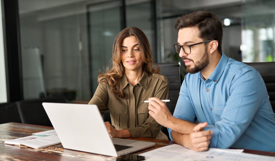 Ein Mann und eine Frau arbeiten gemeinsam konzentriert an einem Laptop und besprechen Unterlagen auf dem Tisch.