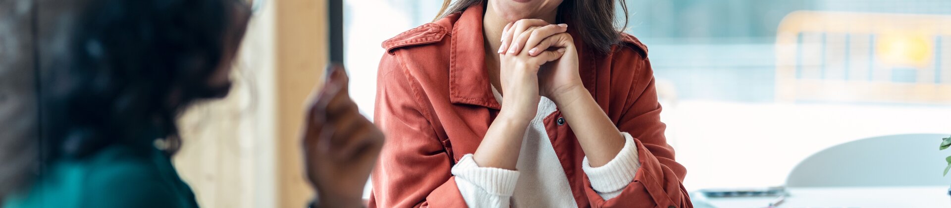 Eine junge Frau sitzt lächelnd in einem Gespräch und wirkt dabei offen und interessiert.