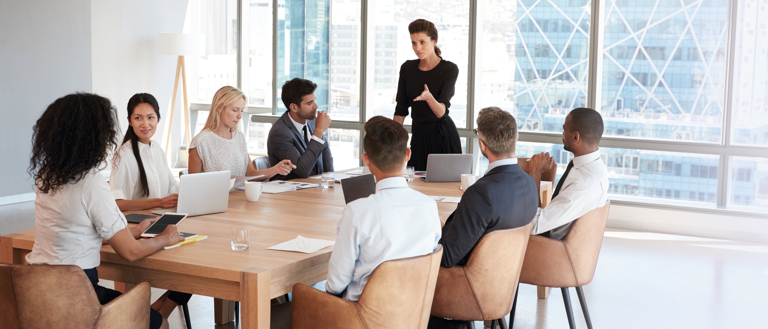 Eine Frau steht vor einer Gruppe von Geschäftspersonen in einem modernen Konferenzraum und leitet eine Besprechung – Symbol für Wirtschaftsmediation, Kommunikation und lösungsorientiertes Konfliktmanagement.