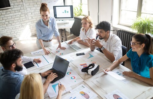 Eine Gruppe von Menschen sitzt an einem Tisch und arbeitet gemeinsam an Laptops und Unterlagen – Symbol für Teamarbeit, Austausch und praxisorientiertes Lernen in der Weiterbildung.