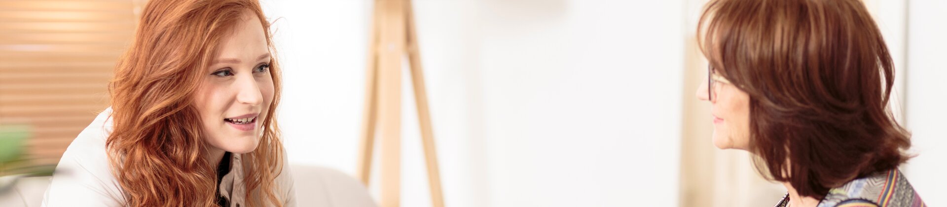 Das Bild zeigt zwei Frauen, die sich in einer ruhigen Umgebung gegenübersitzen und in ein vertrautes Gespräch vertieft wirken.