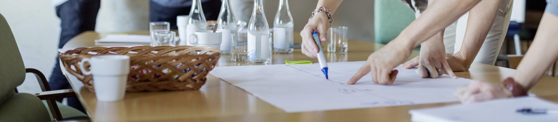 Mehrere Personen arbeiten gemeinsam an Ideen, wobei einige am Tisch skizzieren und andere Post-its an einer Wand anbringen.