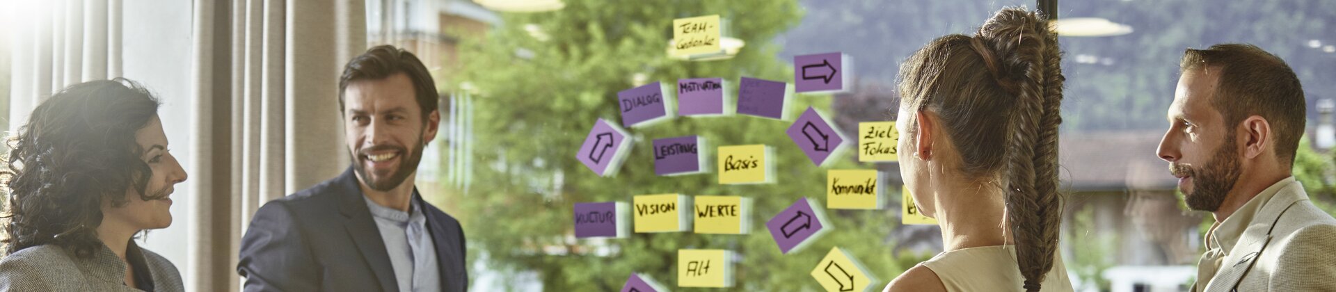 Eine vierköpfige Gruppe hält einen kreativen Workshop vor einer Glaswand voller bunter Haftnotizen.