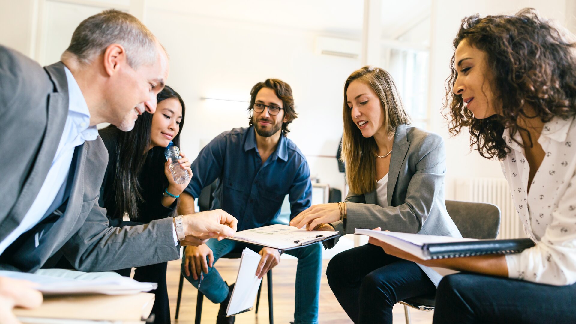 Eine Gruppe von fünf Personen sitzt in einem Kreis und arbeitet konzentriert gemeinsam an Unterlagen.
