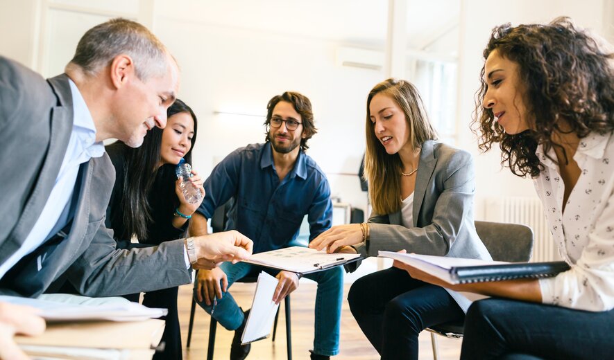 Eine Gruppe von fünf Personen sitzt in einem Kreis und arbeitet konzentriert gemeinsam an Unterlagen.