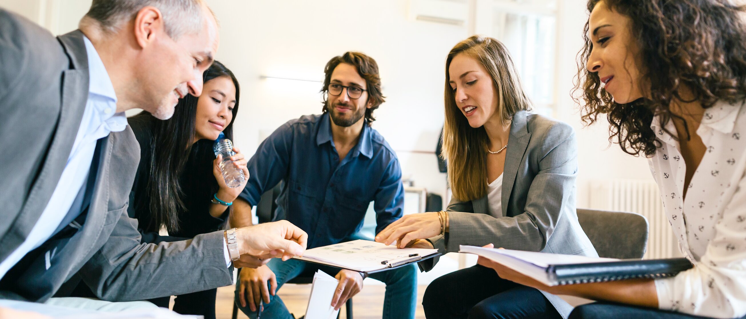Eine Gruppe von Menschen sitzt in einem hellen Seminarraum und diskutiert engagiert – Symbol für Coaching, persönliche Entwicklung und professionellen Austausch auf Augenhöhe.