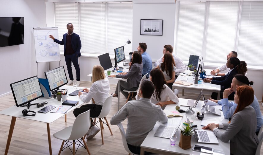 Ein Mitarbeiter präsentiert seinem Team Diagramme und Daten auf einem Flipchart, während alle aufmerksam zuhören.