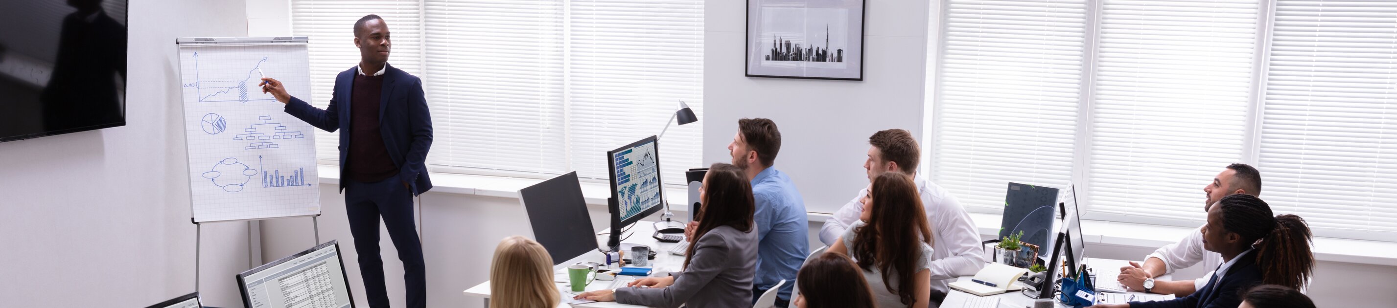 Ein Mitarbeiter präsentiert seinem Team Diagramme und Daten auf einem Flipchart, während alle aufmerksam zuhören.