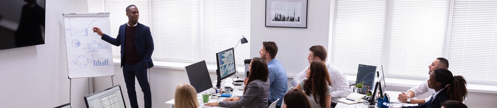 Ein Mitarbeiter präsentiert seinem Team Diagramme und Daten auf einem Flipchart, während alle aufmerksam zuhören.