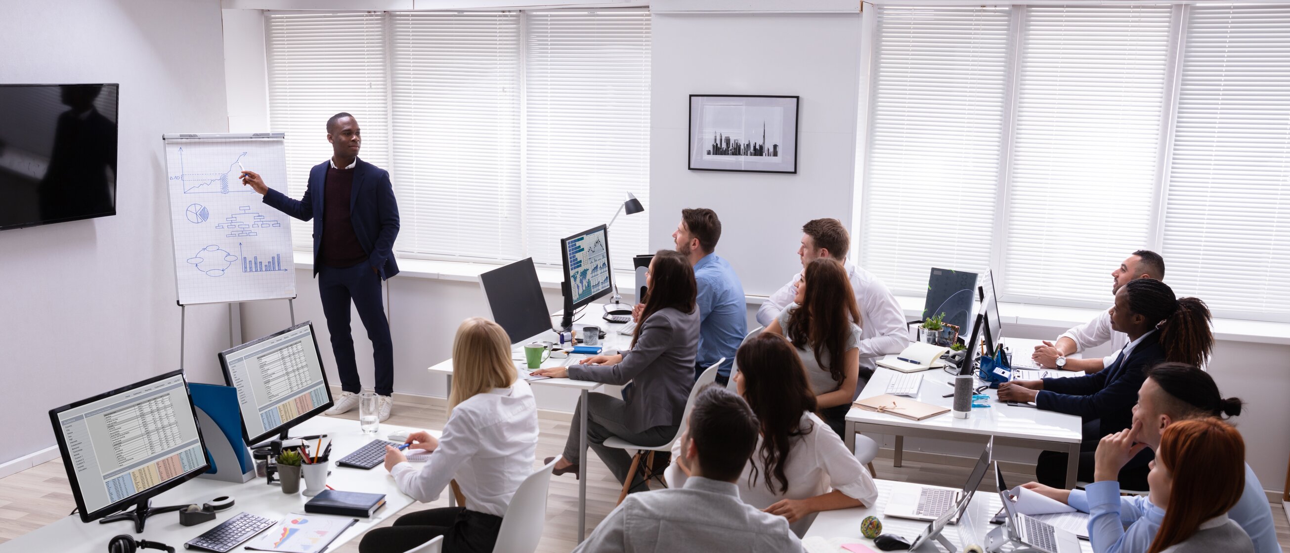 Trainer führt Seminarteilnehmende durch eine Präsentation im modernen Schulungsraum – Weiterbildung zur Persönlichkeitsentwicklung und Kommunikation für mehr Souveränität im Beruf.