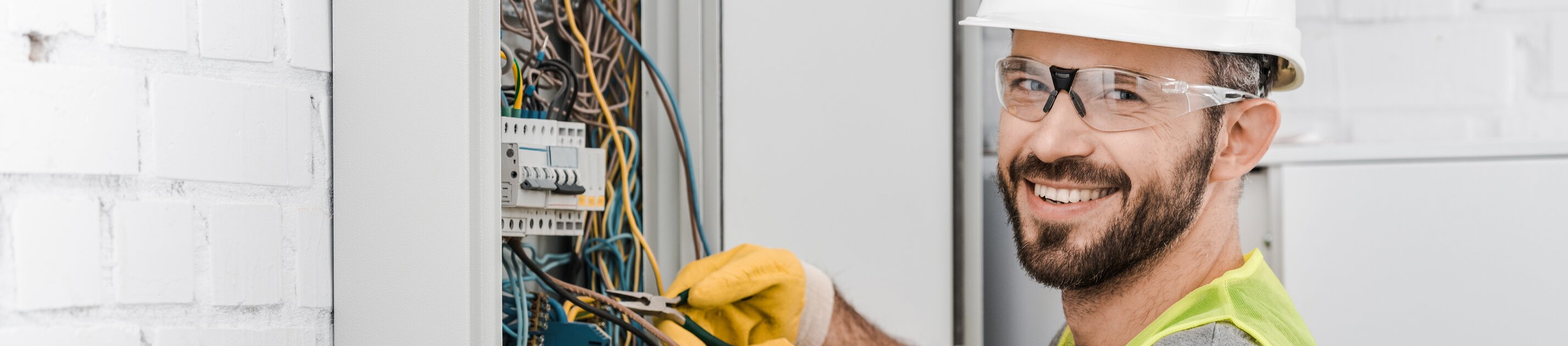 Ein Elektriker arbeitet lächelnd an einem offenen Schaltschrank voller Kabel.