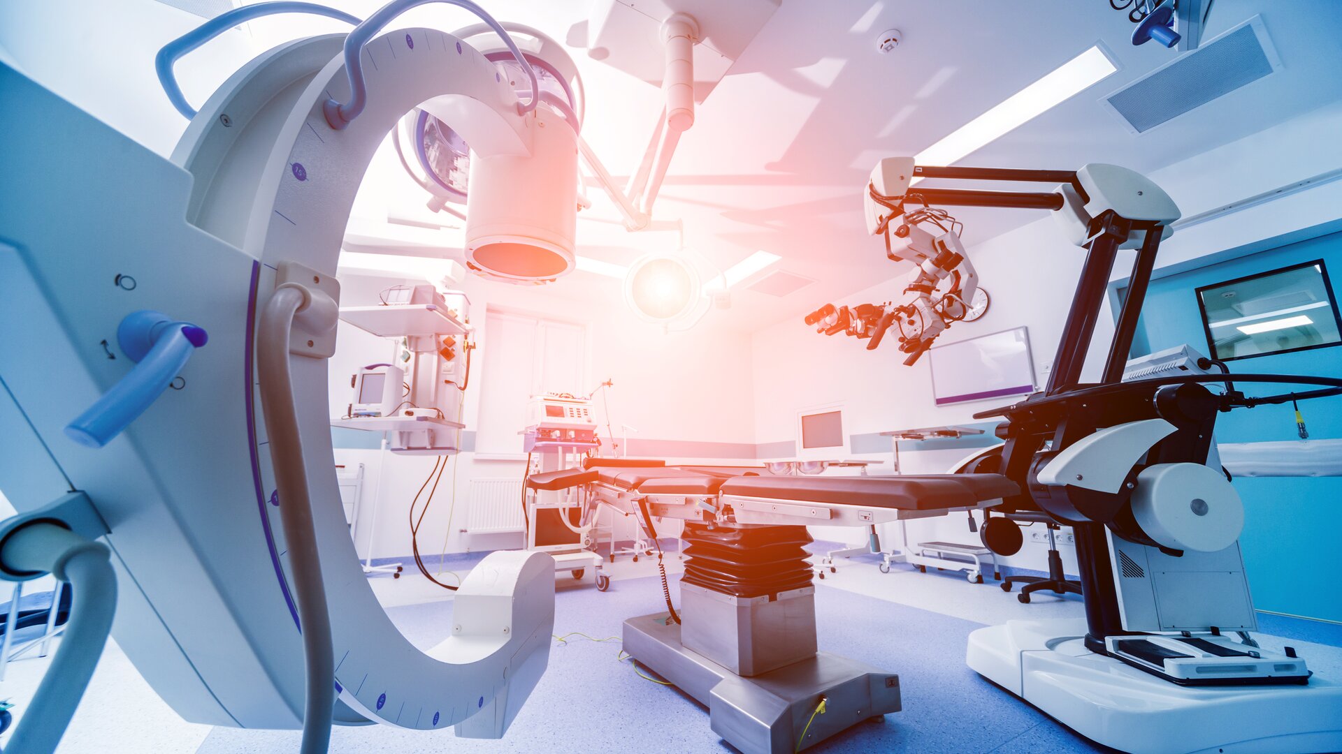 Ein hochmodern ausgestatteter Operationssaal mit robotergestützter Medizintechnik und bildgebenden Geräten.