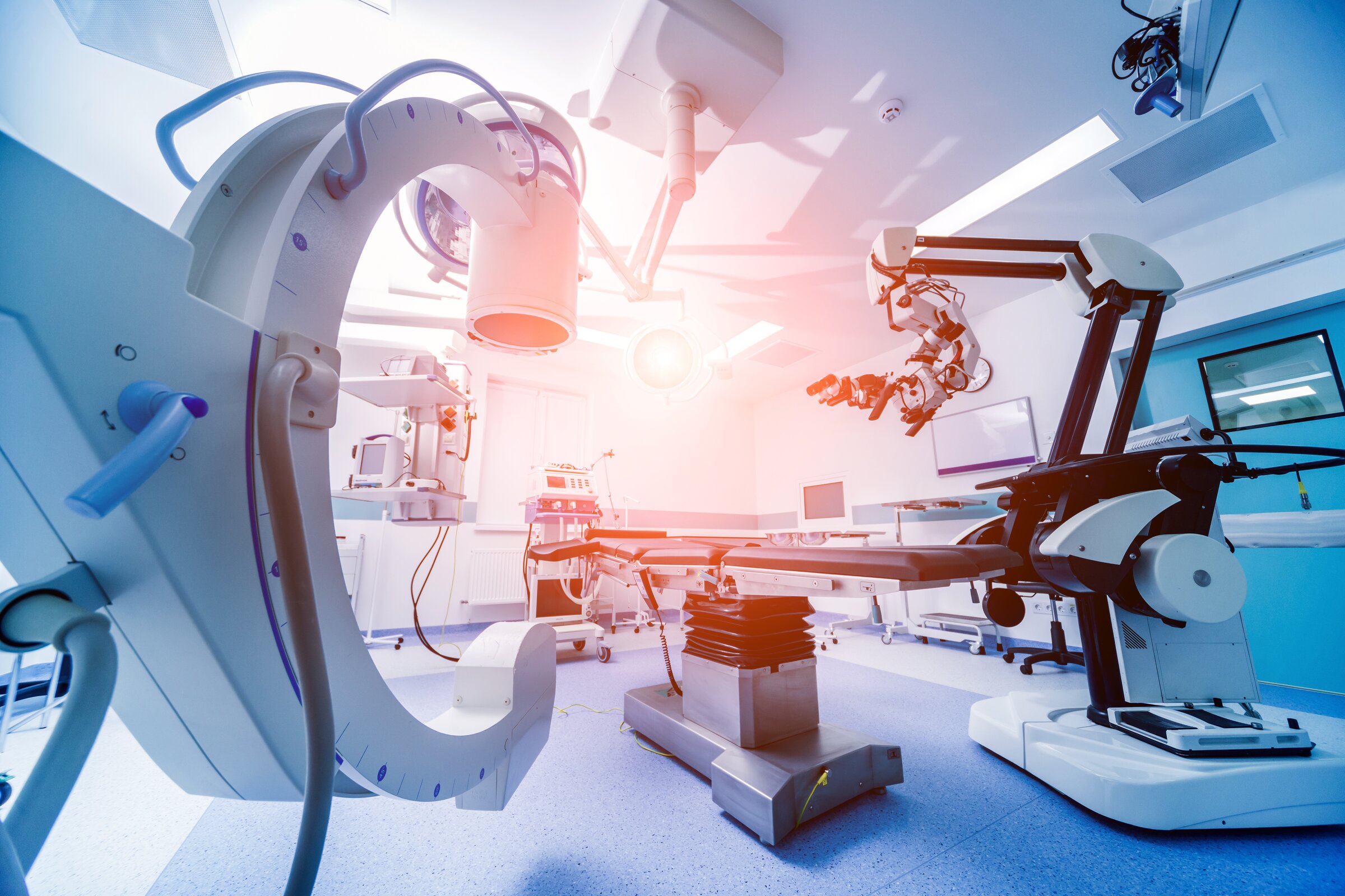 Ein hochmodern ausgestatteter Operationssaal mit robotergestützter Medizintechnik und bildgebenden Geräten.