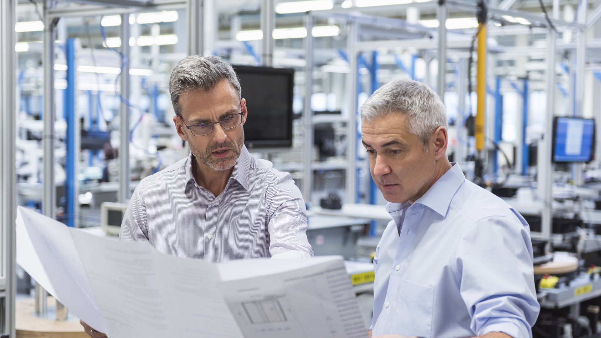 Zwei Ingenieure besprechen konzentriert technische Pläne in einer Produktionshalle.
