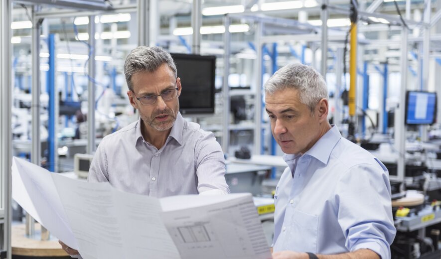 Zwei Ingenieure besprechen konzentriert technische Pläne in einer Produktionshalle.