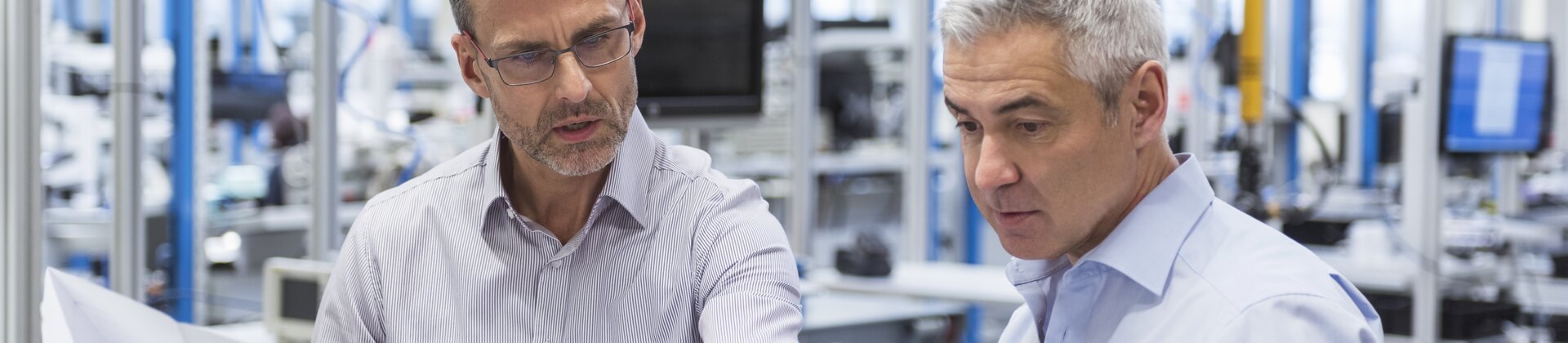 Zwei Ingenieure besprechen konzentriert technische Pläne in einer Produktionshalle.