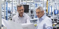 Zwei Ingenieure besprechen konzentriert technische Pläne in einer Produktionshalle.