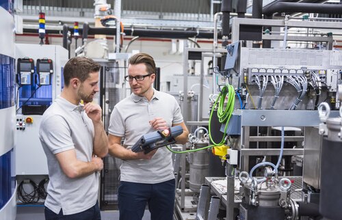 Gepr. Industriemeister Elektrotechnik diskutieren in einer Halle über ein Messergebnis. 