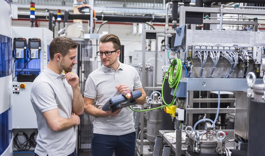 Zwei Techniker stehen in einer modernen Industrieanlage und prüfen gemeinsam die Einstellungen einer Maschine.