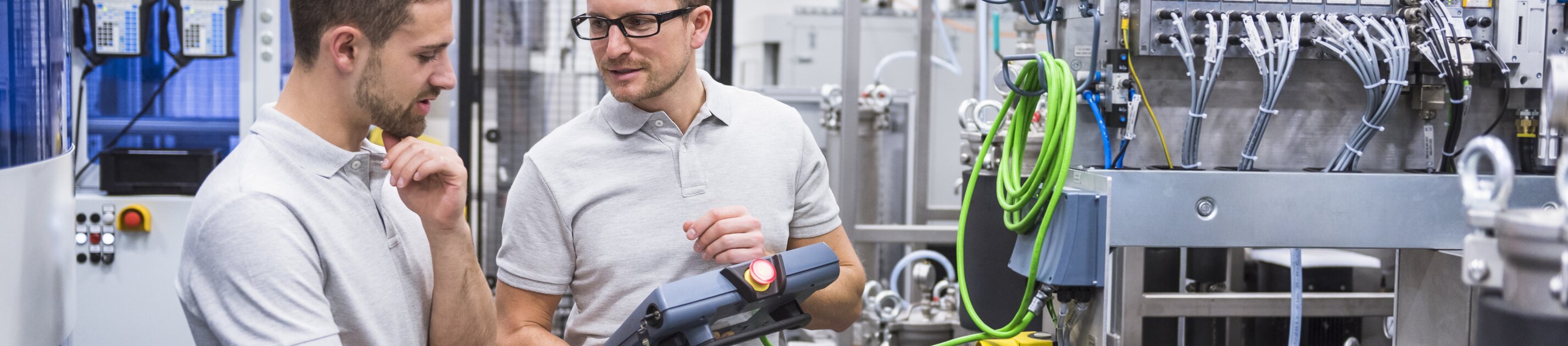 Zwei Techniker stehen in einer modernen Industrieanlage und prüfen gemeinsam die Einstellungen einer Maschine.