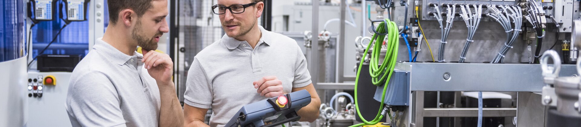 Zwei Techniker stehen in einer modernen Industrieanlage und prüfen gemeinsam die Einstellungen einer Maschine.