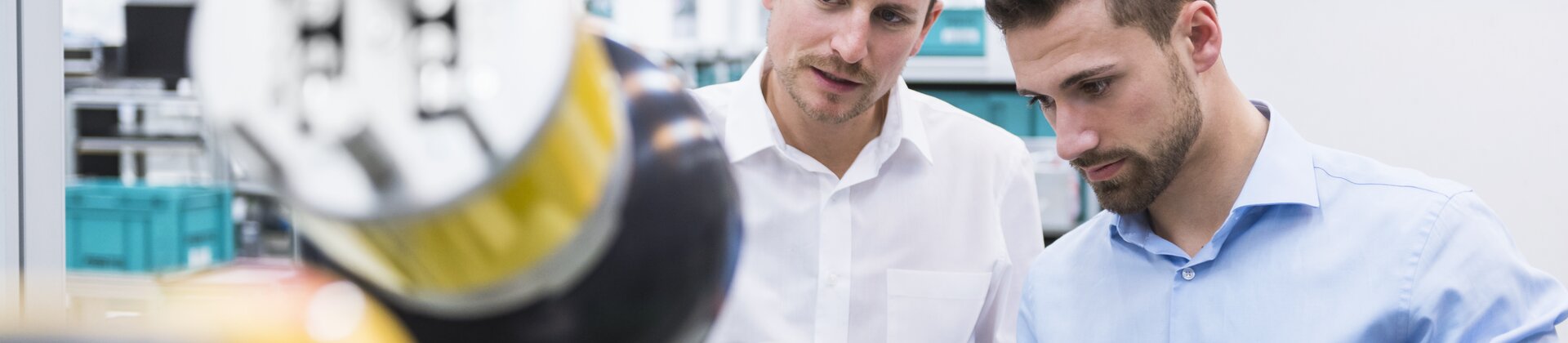 Zwei Mitarbeiter prüfen gemeinsam eine Maschine und vergleichen deren Daten auf einem Tablet.