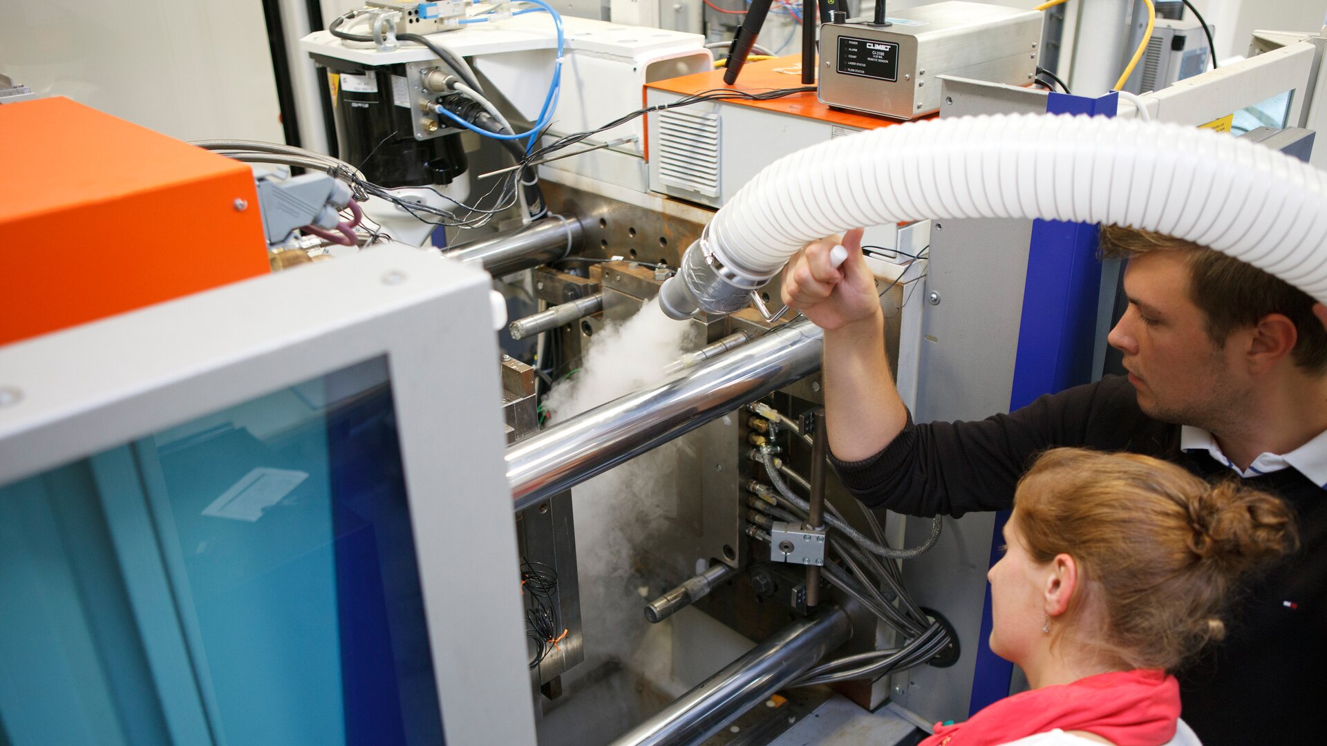 Zwei Personen überprüfen gemeinsam eine Maschine, während ein Kühl- oder Dampfprozess sichtbar aktiv ist.