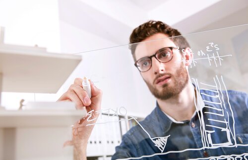 Ein Mann zeichnet technische Diagramme auf eine transparente Tafel – Symbol für strategisches Denken, Planung und technische Führungsverantwortung.