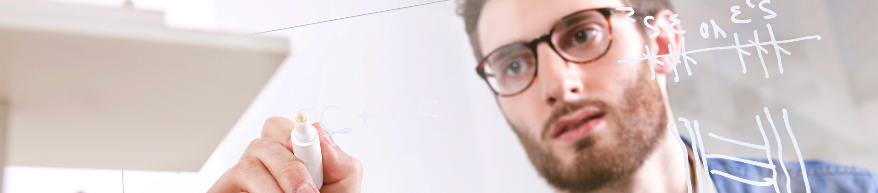 Ein konzentrierter Mann skizziert Diagramme und Formeln auf einer transparenten Tafel.