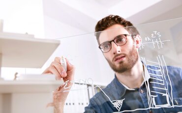 Technische Weiterbildungen: Ein Mann zeichnet etwas technisches auf ein durchsichtiges Board. 