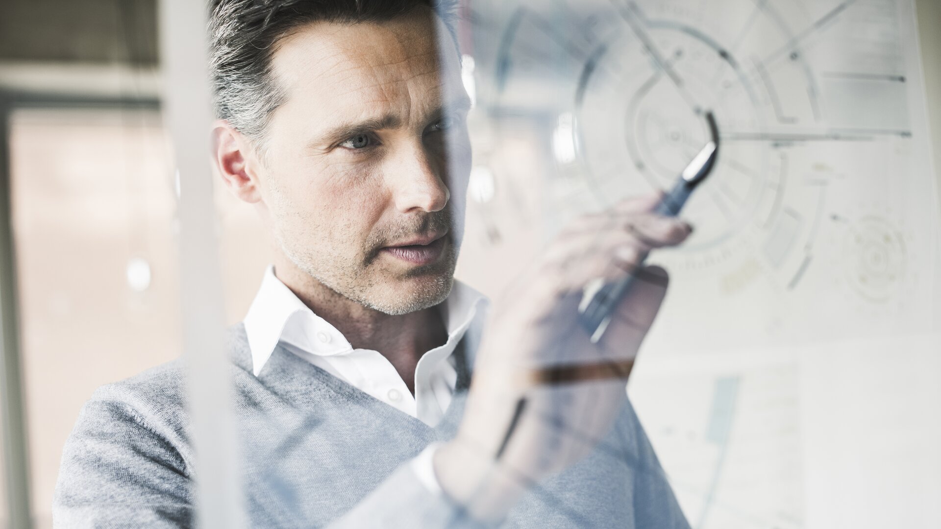 Ein Mann zeichnet konzentriert Diagramme und Notizen auf eine transparente Tafel.