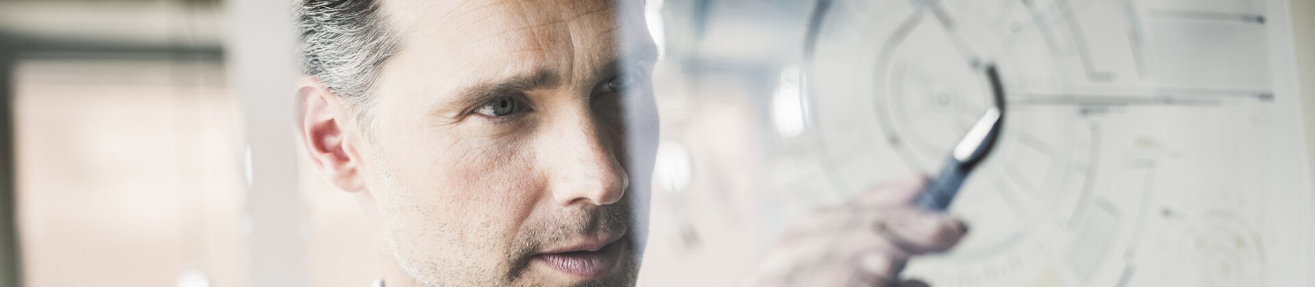 Ein Mann zeichnet konzentriert Diagramme und Notizen auf eine transparente Tafel.