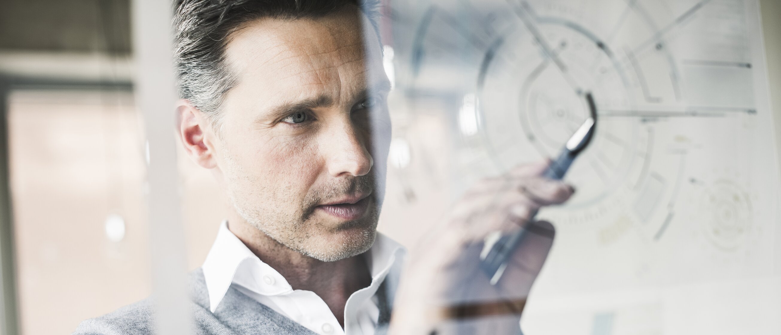 Ein Mann zeichnet konzentriert Diagramme und Notizen auf eine transparente Tafel.