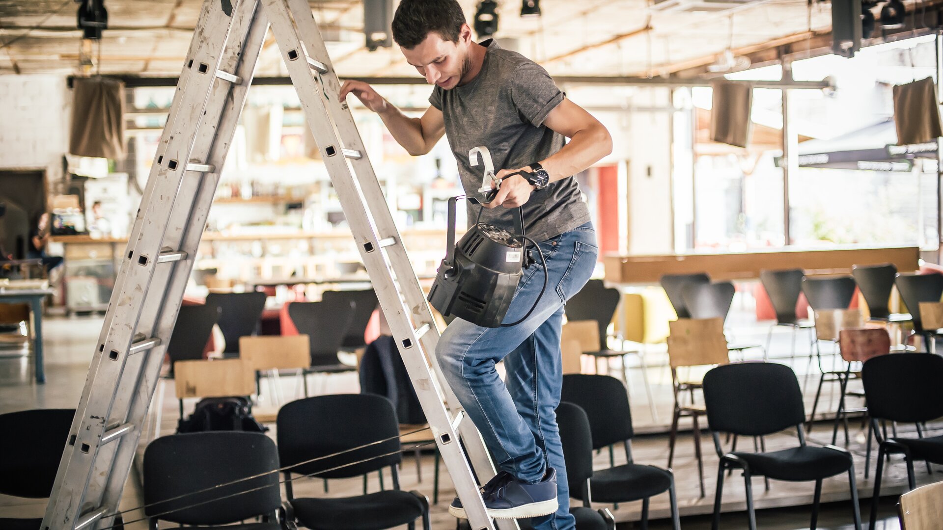 Ein Mann steigt eine Leiter hinauf, um in einem Veranstaltungsraum technische Geräte zu installieren.