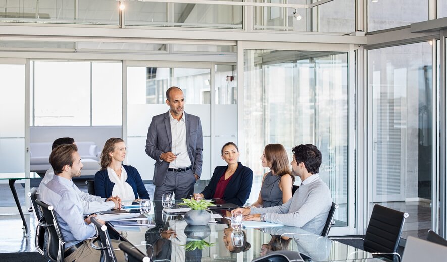 Ein Team sitzt im modernen Konferenzraum zusammen, während ein Mann im Anzug die Besprechung leitet.