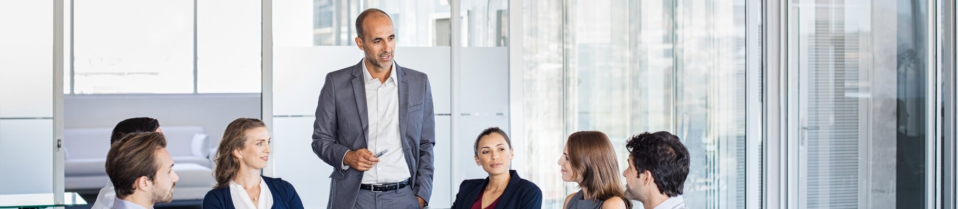 Ein Team sitzt im modernen Konferenzraum zusammen, während ein Mann im Anzug die Besprechung leitet.