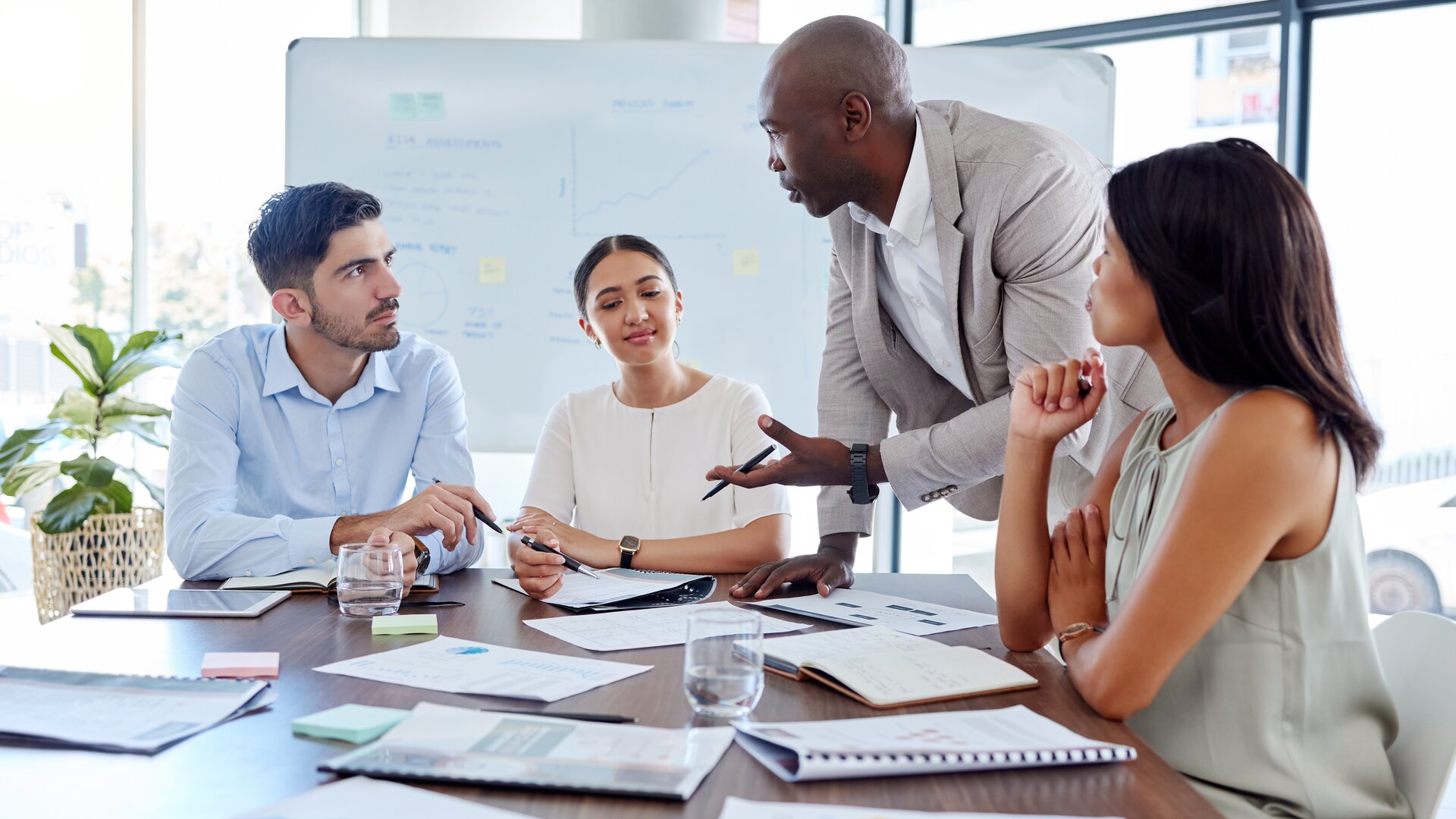 Ein Team sitzt zusammen im Meeting, während ein stehender Kollege engagiert etwas erklärt.