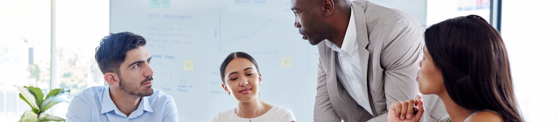 Ein Team sitzt zusammen im Meeting, während ein stehender Kollege engagiert etwas erklärt.