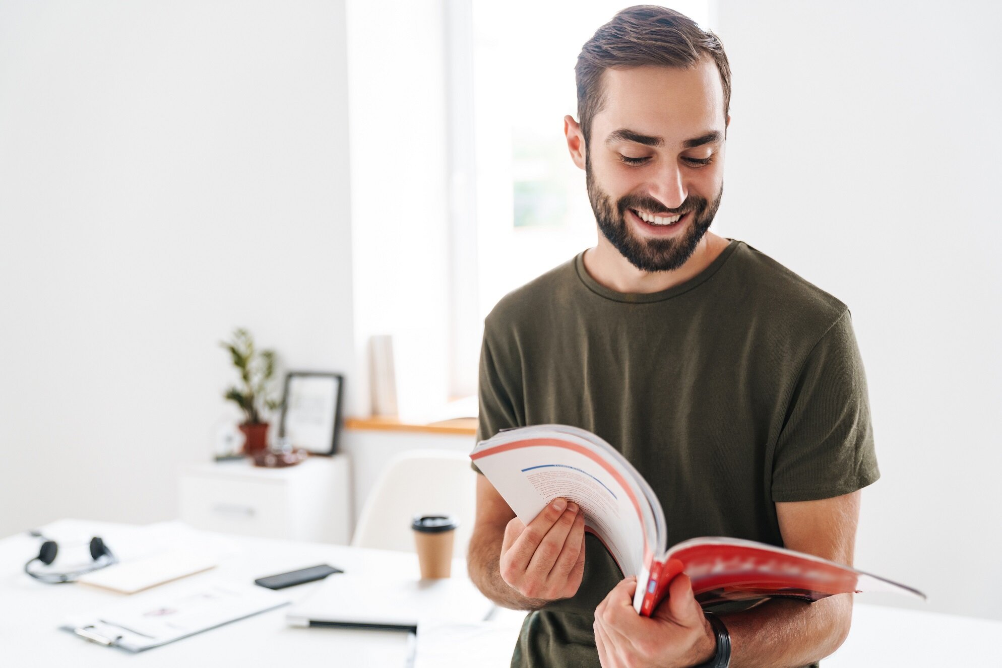 Junger Mann sitzt am Schreibtisch, liest konzentriert in einem Buch und lächelt – Symbol für Weiterbildung und nächste Karriereschritte nach dem Abschluss als Geprüfte/-r Industriefachwirt/-in.