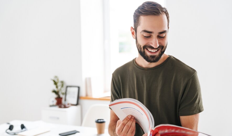 Ein junger Mann liest gut gelaunt in einer Broschüre.
