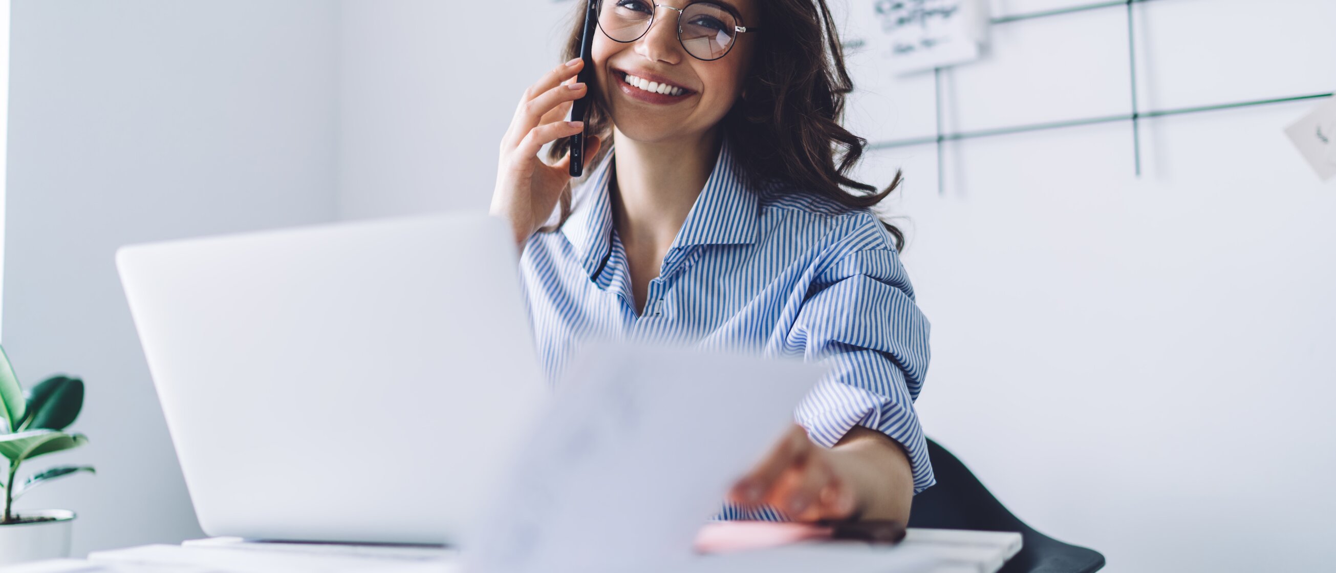 Eine junge Frau arbeitet gut gelaunt am Laptop und telefoniert gleichzeitig.