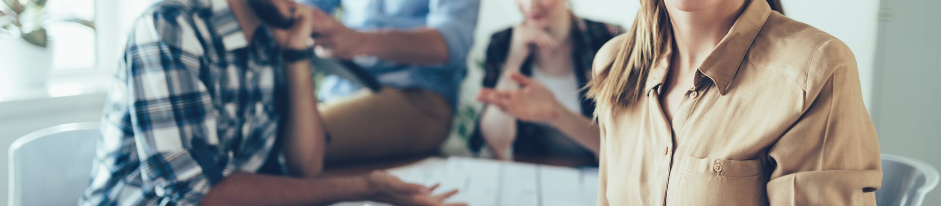 Eine Gruppe junger Fachleute arbeitet gemeinsam an Projekten, während eine lächelnde Frau im Vordergrund ein Tablet hält.