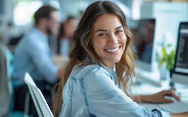 Junge Frau lächelt im modernen Büro vor dem Computer – Übersicht zu allen IHK-Fachkraft Weiterbildungen