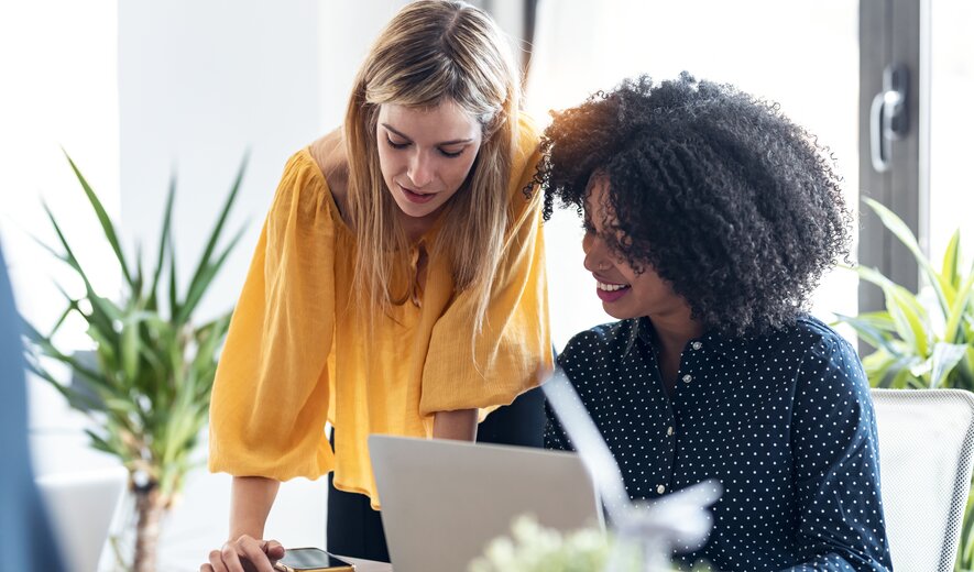Zwei Kolleginnen arbeiten konzentriert gemeinsam an einem Projekt und tauschen sich dabei über Ideen und Inhalte aus.