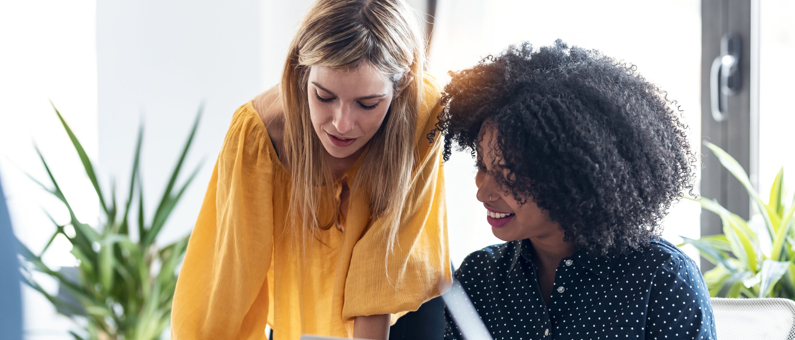 Zwei Kolleginnen arbeiten konzentriert gemeinsam an einem Projekt und tauschen sich dabei über Ideen und Inhalte aus.