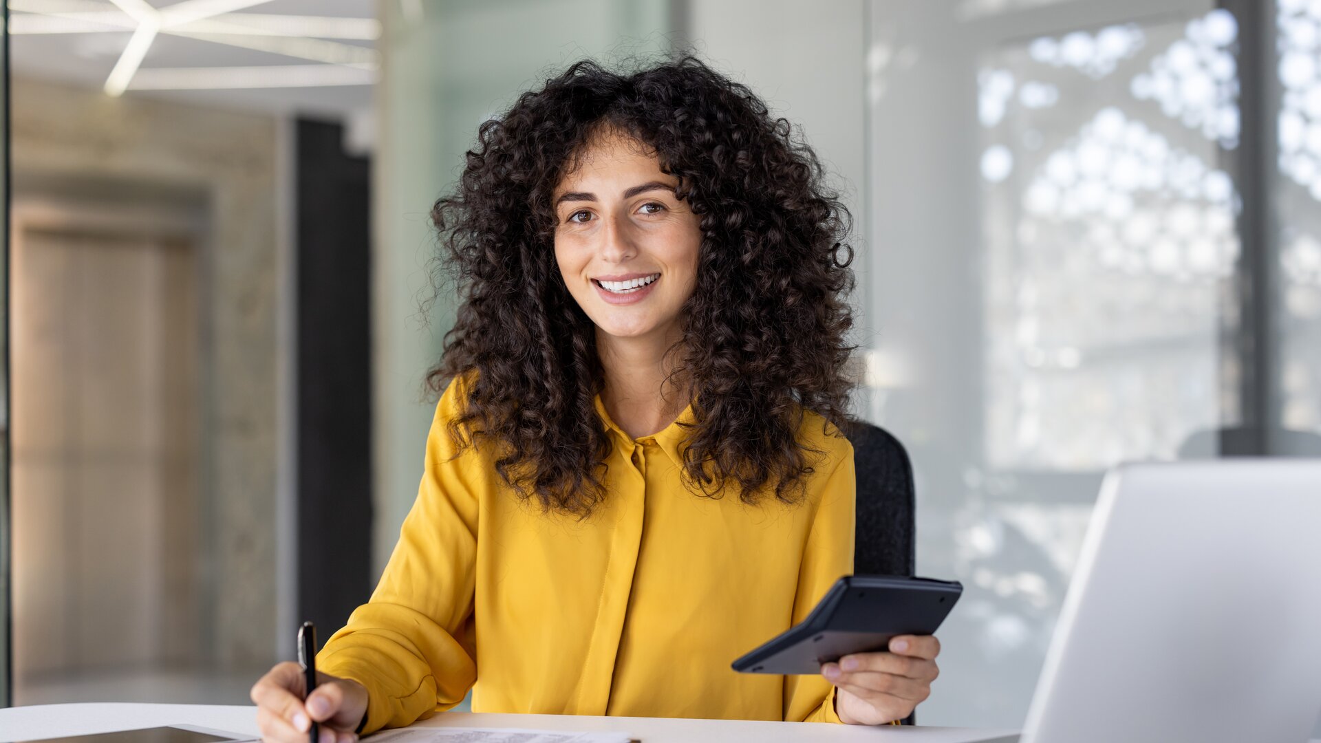 Eine junge Frau arbeitet lächelnd im Büro und wirkt konzentriert bei der Bearbeitung ihrer Unterlagen.