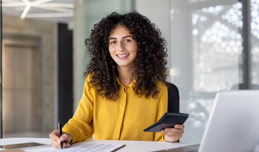 Eine junge Frau arbeitet lächelnd im Büro und wirkt konzentriert bei der Bearbeitung ihrer Unterlagen.